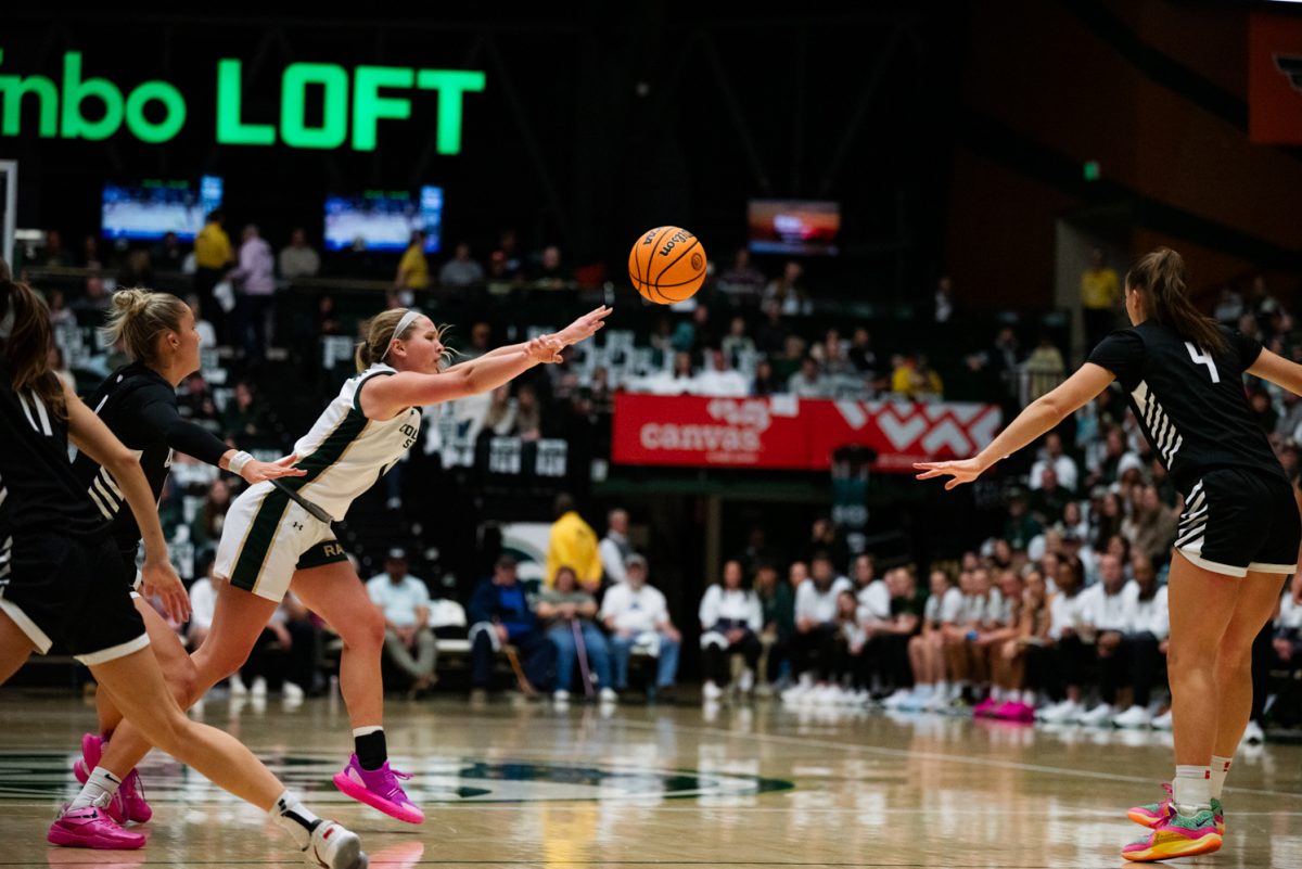 A female basketball player in white and green leans over and throws a basketball while surrounded by defenders in black and white.