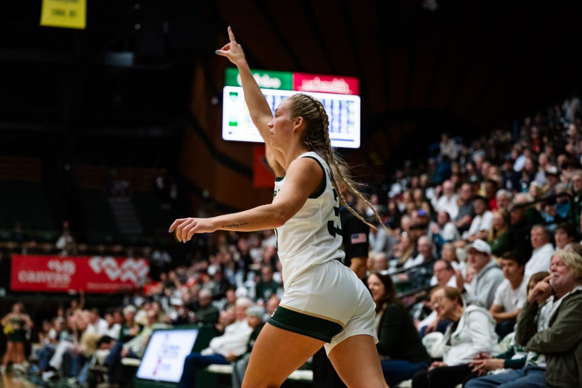 A female basketball player in white and green points up while running.