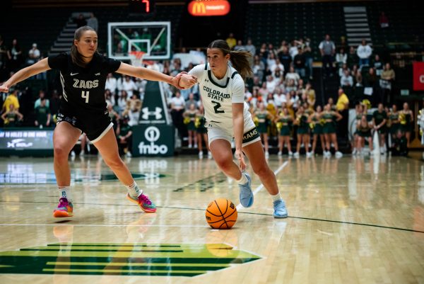 A female basketball player in white and green dribbles a basketball while a player in black and white pushes into her.