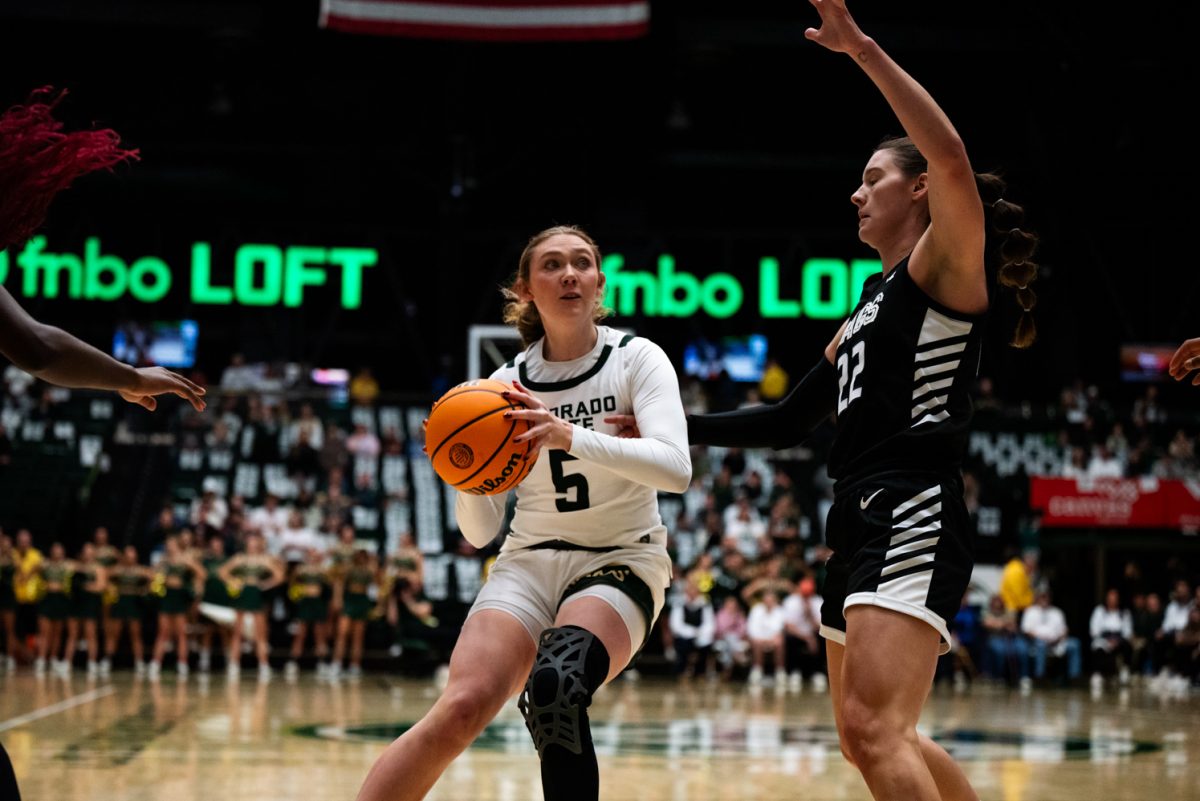 A female basketball player in white and green guards the basketball in her hands from a player in black and white.