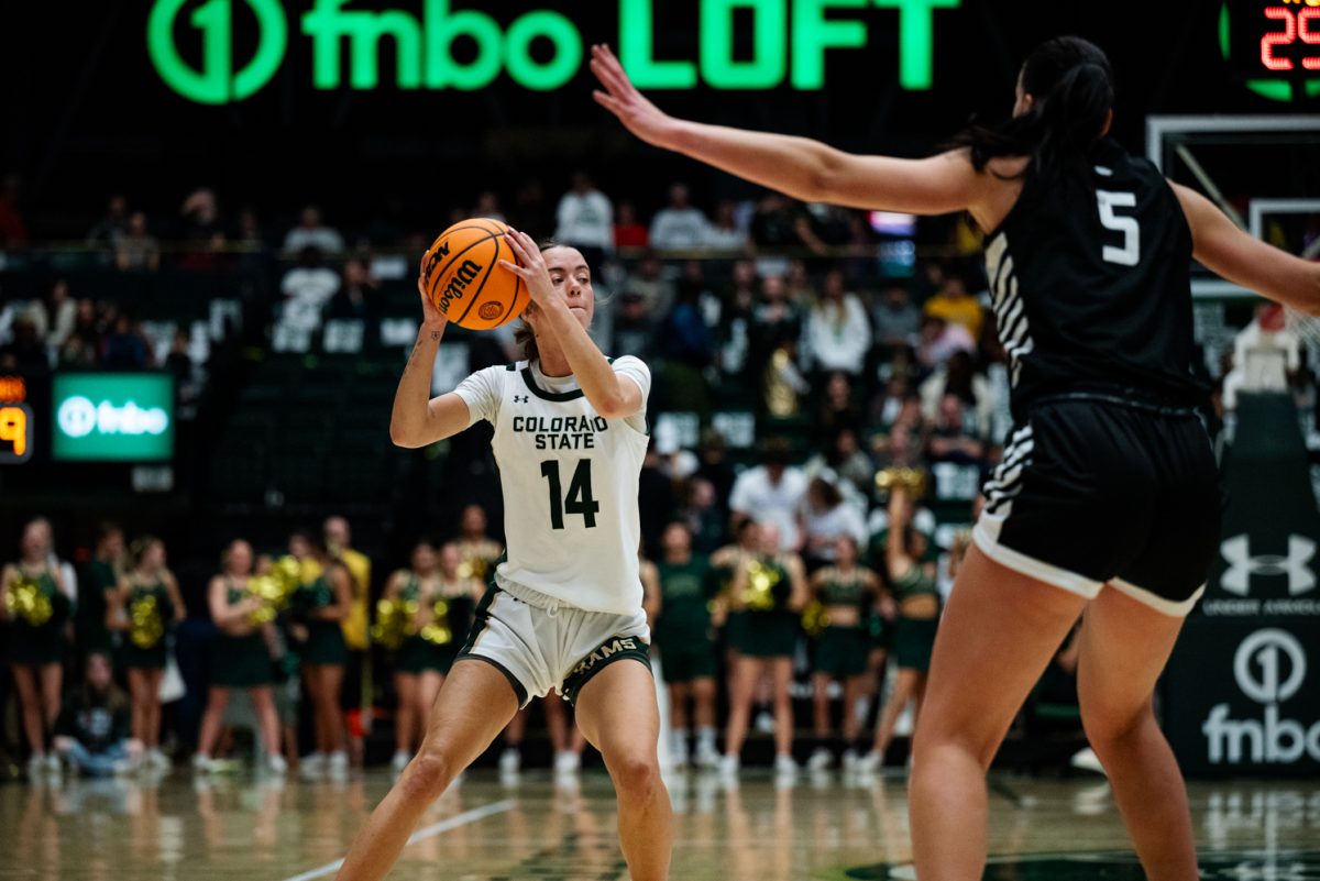 A female basketball player in white and green holds a basketball by her face. A player in black and white defends her in the foreground.