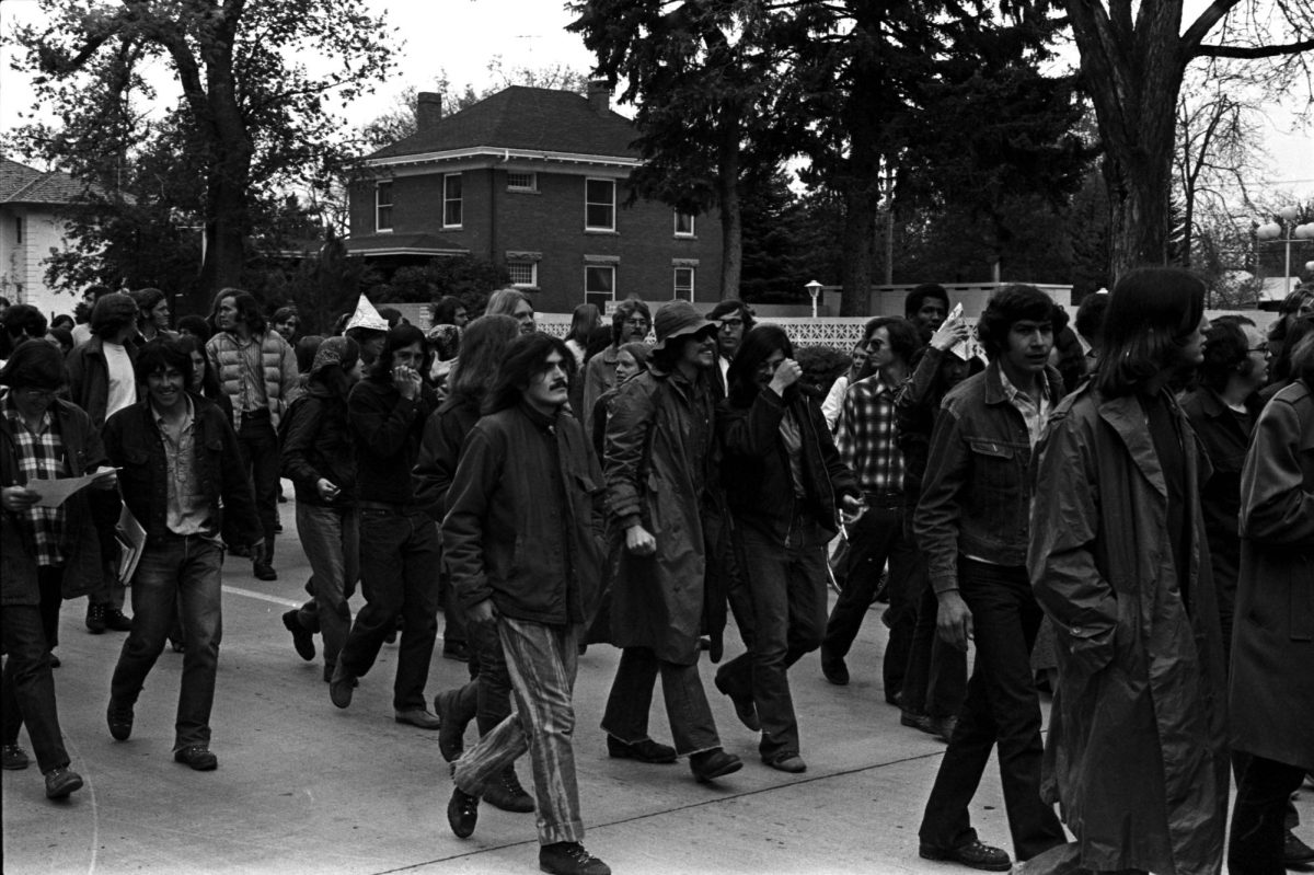 A black and white photo of a crowd of people walking down a suburban street.