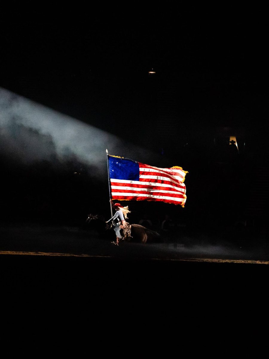 A woman rides a horse while holding an American flag