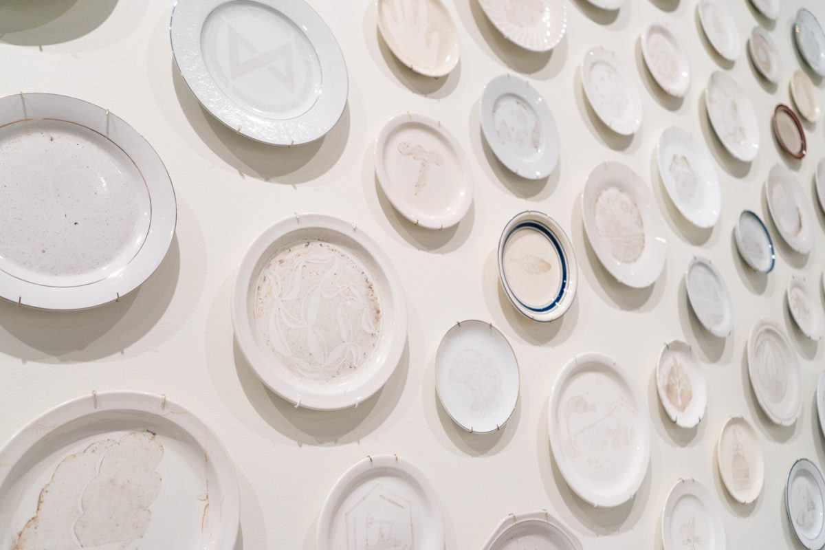 Image of student-designed plates hanging on the wall at the "Community Smog" exhibition by Kim Abeles at the Gregory Allicar Museum of Art in the University Center for the Arts.