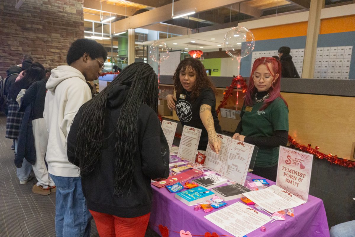 Two people stand behind a table talking while two others stand in front of the table listening.