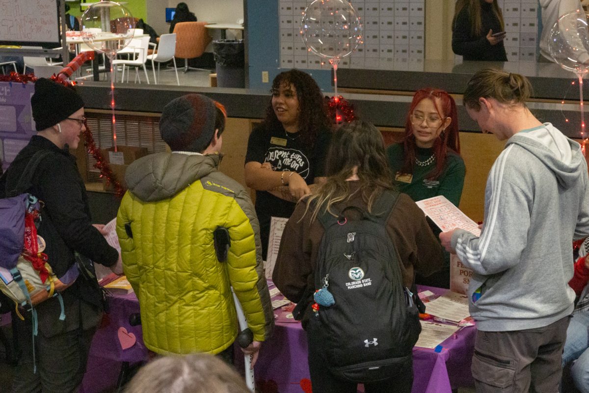 Two people stand behind a table talking to four people in front of the table.