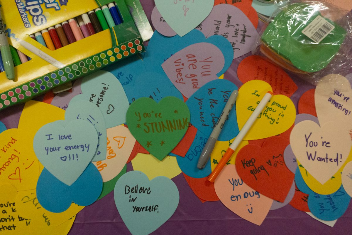 Paper hearts with words on them sit on a table along with markers.