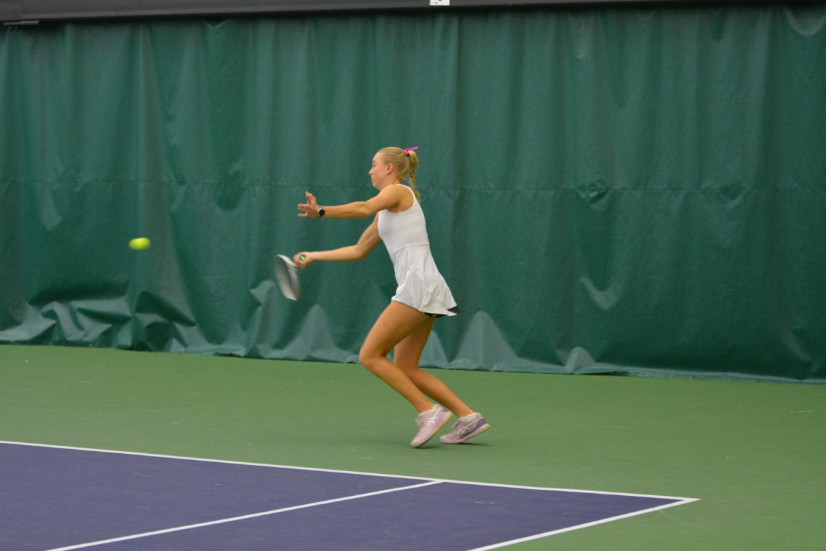 Girl in white tennis outfit hits the ball.
