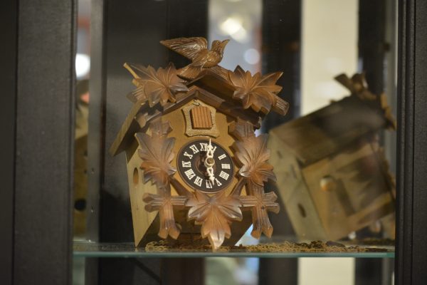 A wooden clock with crosses and leaves in a glass case.