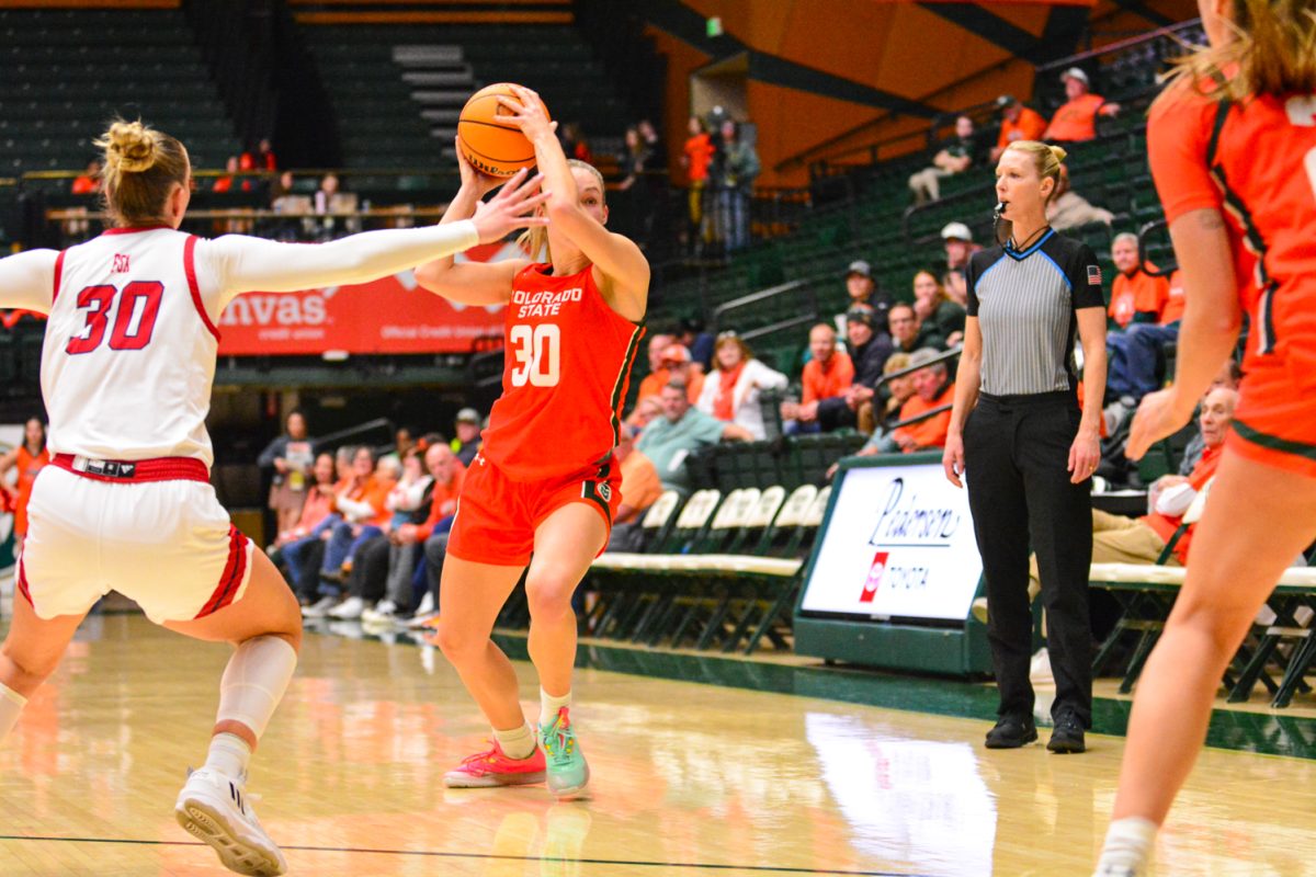 Hannah Ronsiek throwing the ball to her teammates while being guarded by a Fresno State Player Feb. 19. Hannah and her teammates are wearing their orange jerseys during their Aggies game.