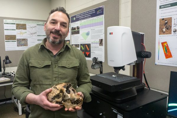 A person stands holding a skull in front of a 3-D scanner.