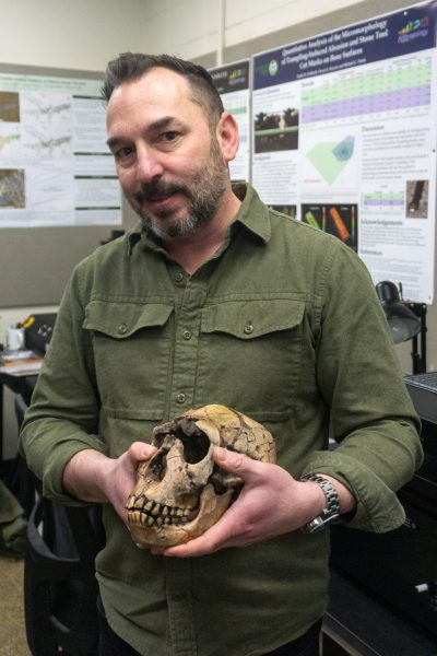 A person stands holding a skull.