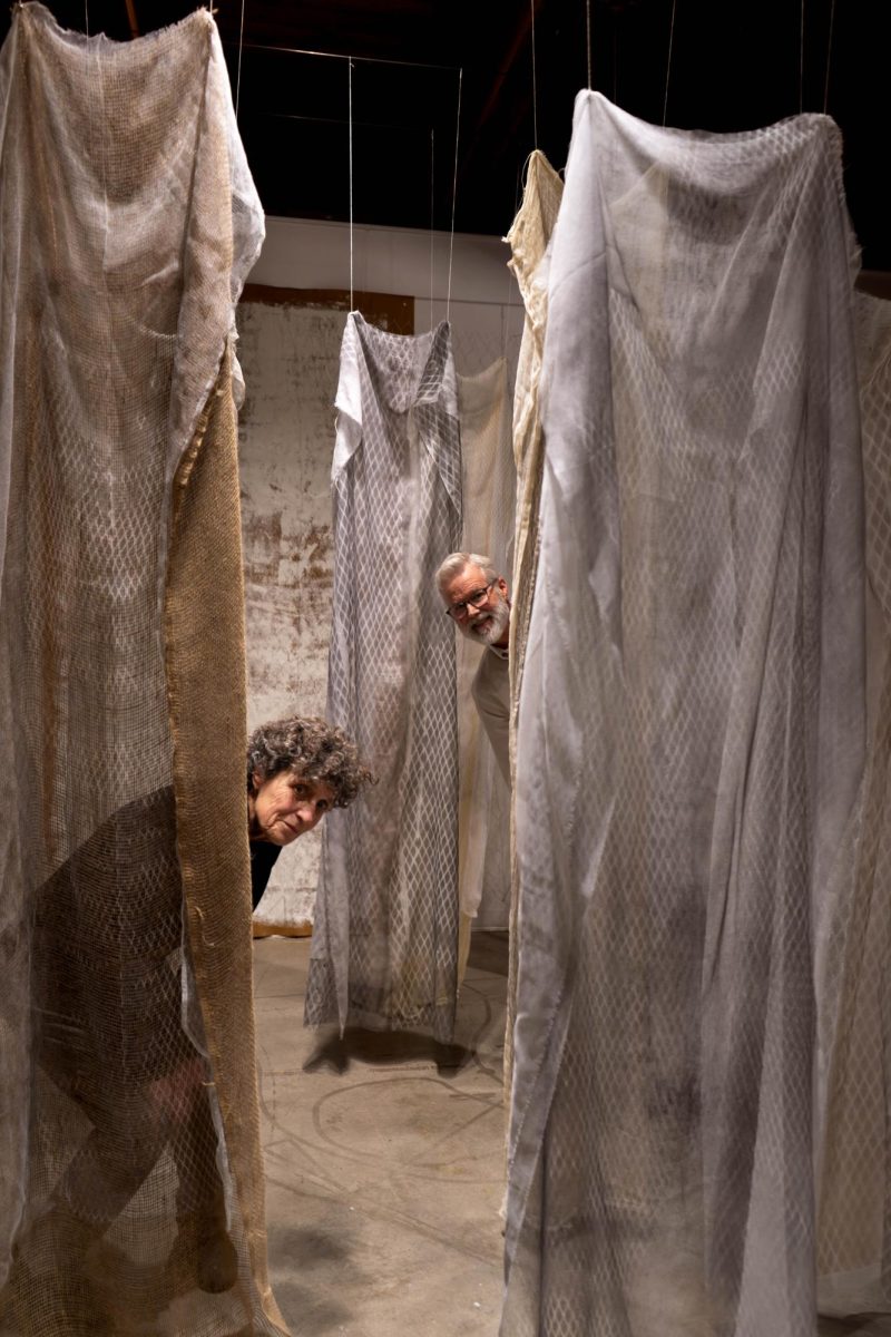 Two people poke their heads out from behind fabrics hanging from the ceiling