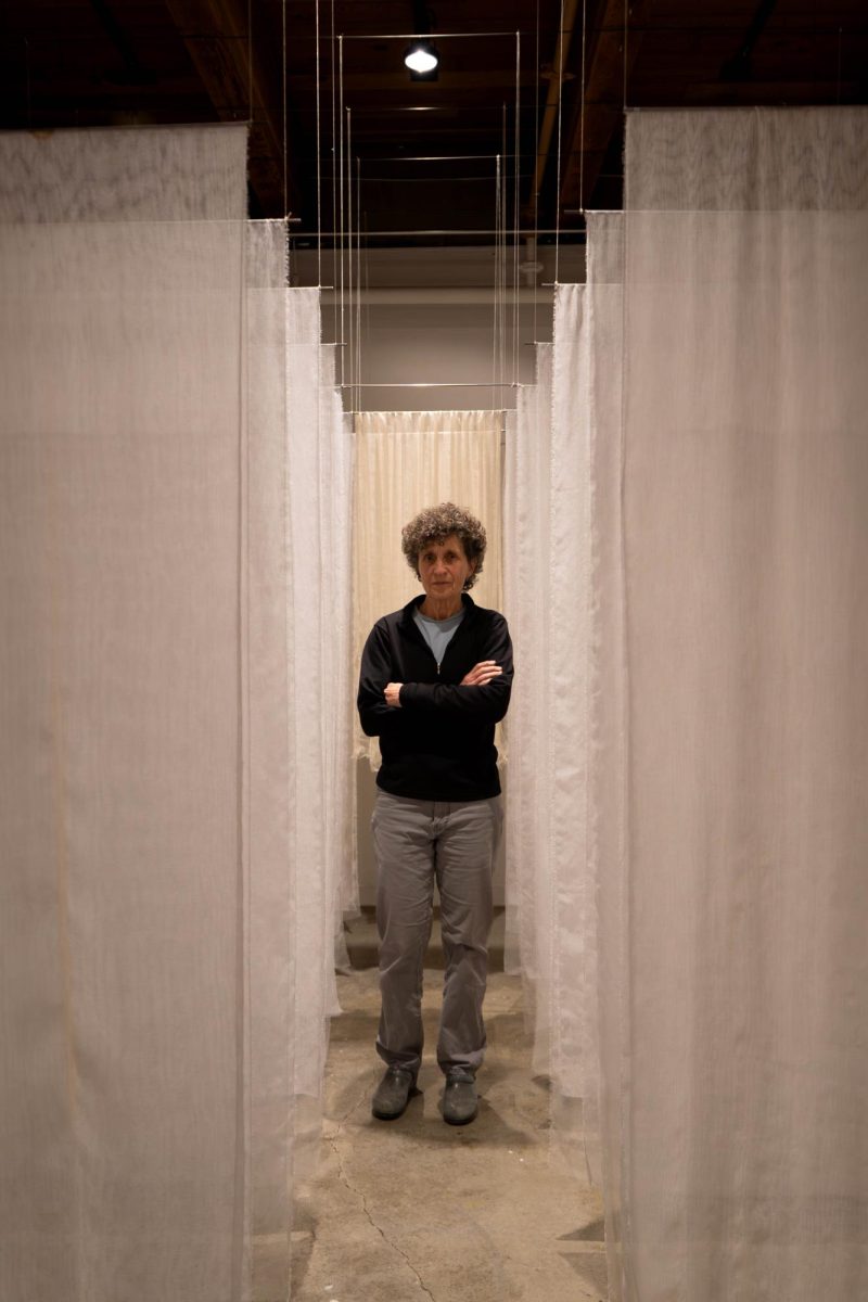 A woman stands in an array of white sheets hanging from the ceiling