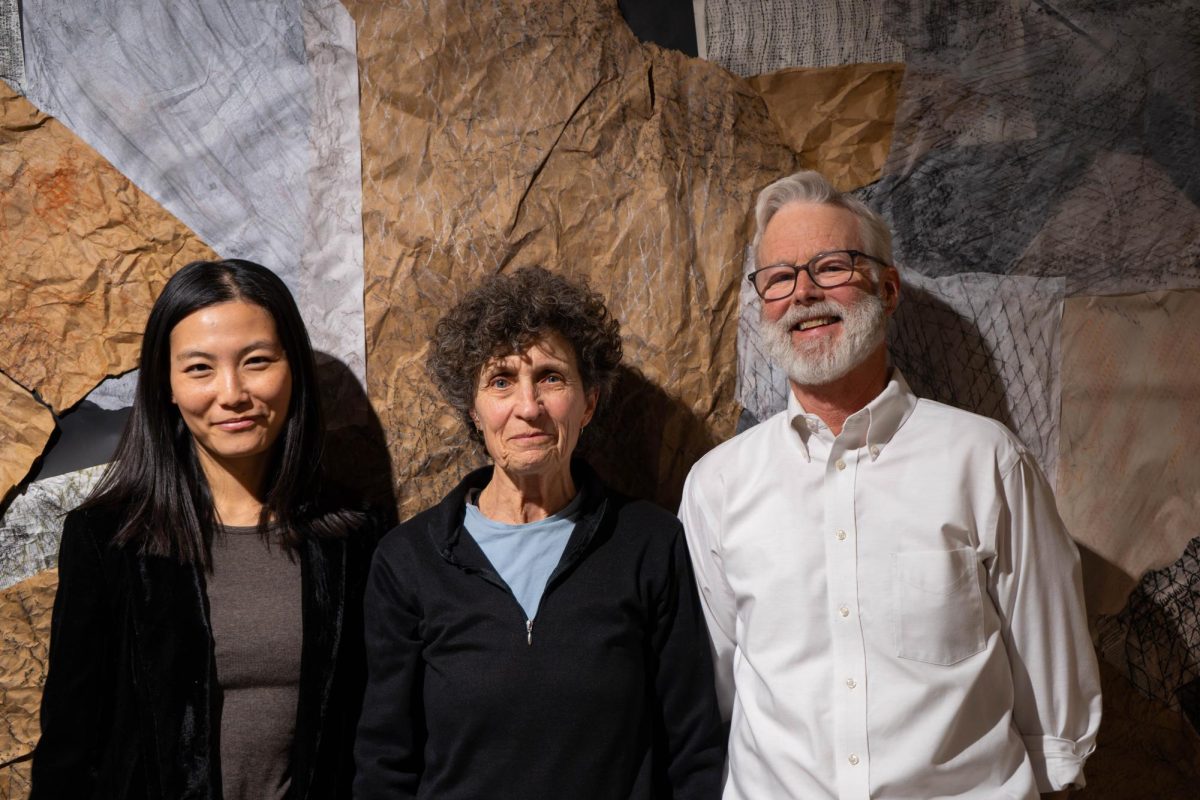 Three people stand in front of a wall covered in interwoven fabric