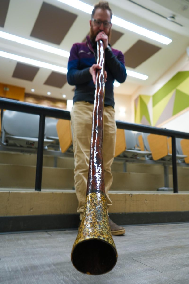 Dr. Robin Rothfeder stands in front of a lecture hall, playing the didgeridoo.