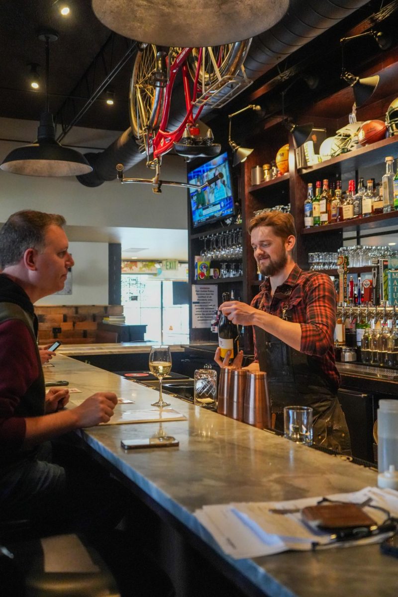 A bartender serves a customer a glass of wine at a bar.