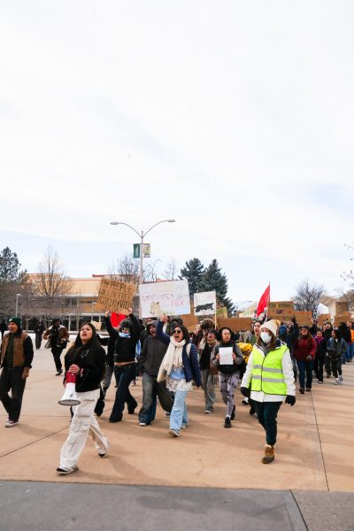 Protestors walk through the LSC plaza, holding signs and flags, chanting.