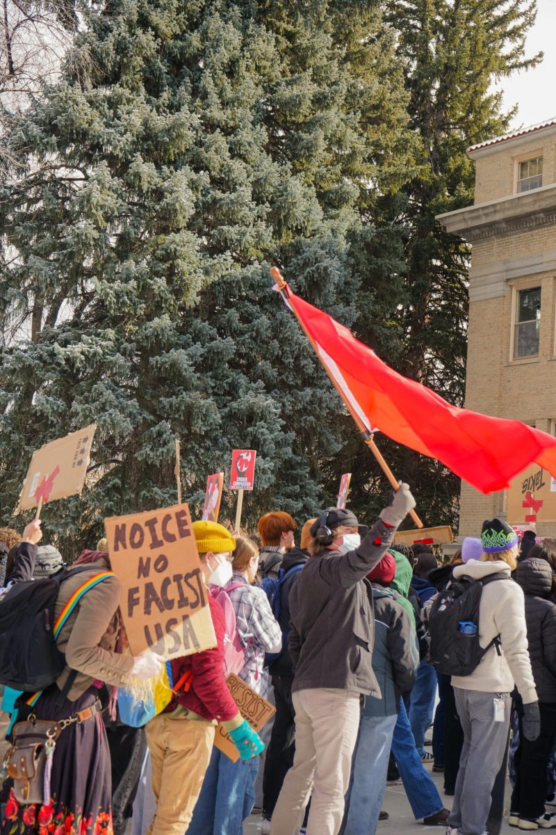The sun comes out on the protestors in front of the CSU administration building. A person waves a red flag and someone holds a sign that reads, "No ICE, no Fascist USA."