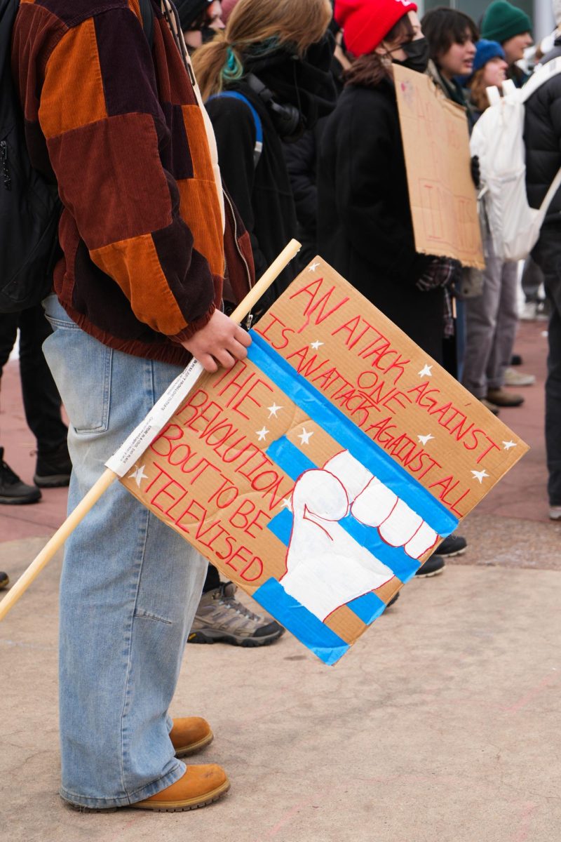 A protester holds a sign that reads, "An attack on one is an attack against all. The revolution 'bout to be televised," in front of the Lory Student Center.