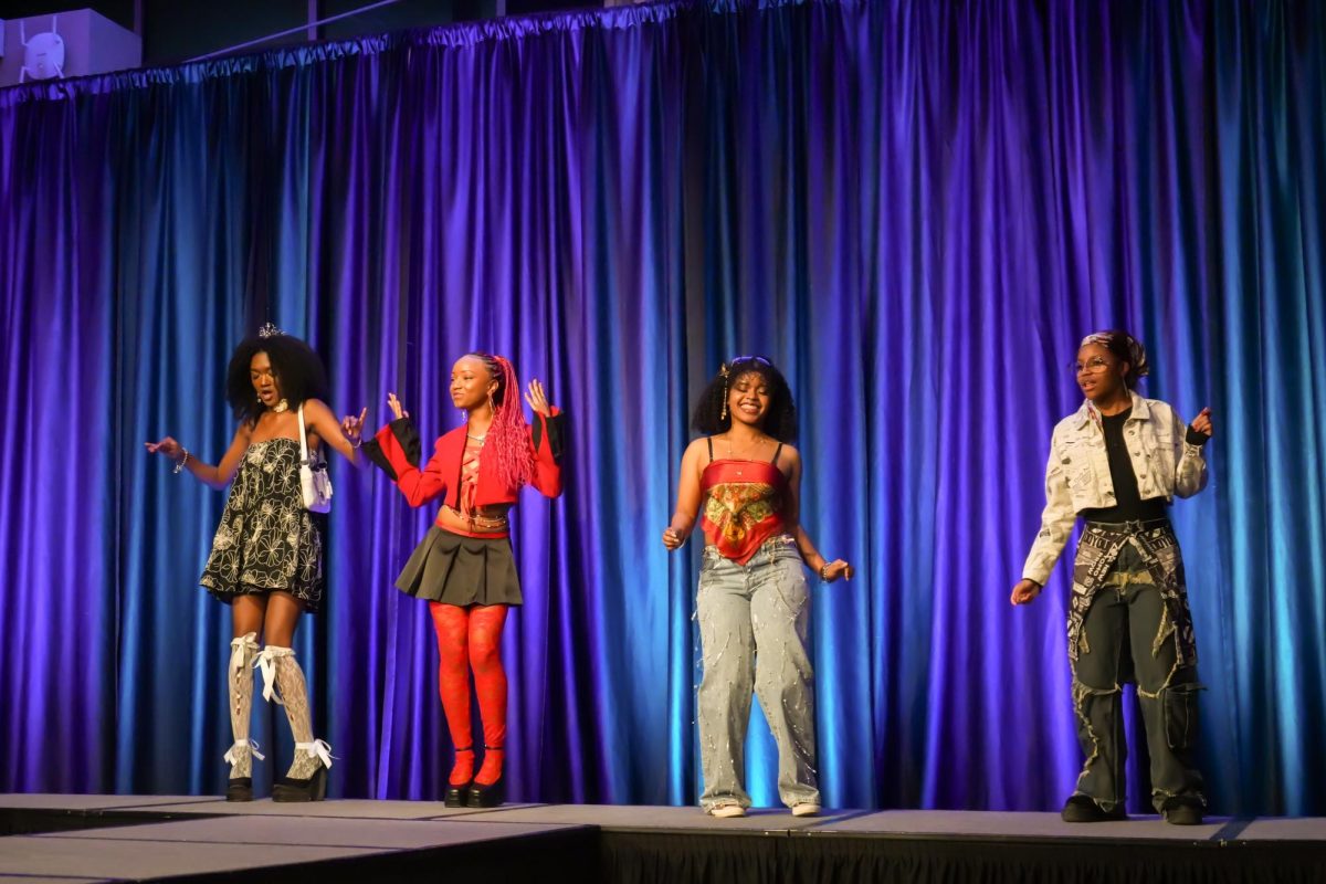 Four fashion models dance on stage in front of a purple curtain.