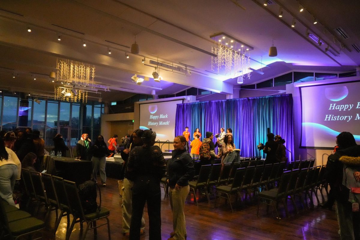 Students mingle in a dark lit room. A projection in the back reads, "Happy Black History Month!"