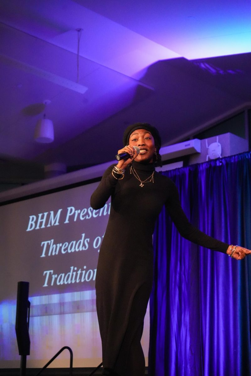 A woman sings into a microphone. A projection behind her reads, "BHM presents: Threads of Tradition."