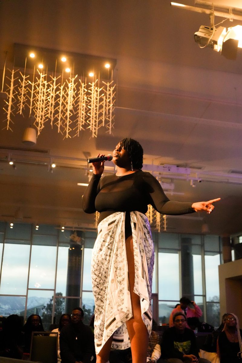 A woman sings into a microphone on the end of a runway stage in front of a crowd.