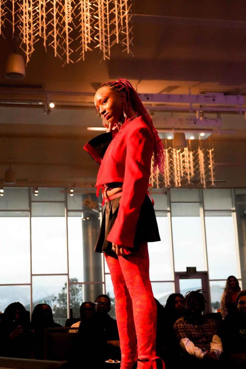 Anaya Ewing stands at the end of a fashion runway wearing a red outfit that matches her red hair and make up.