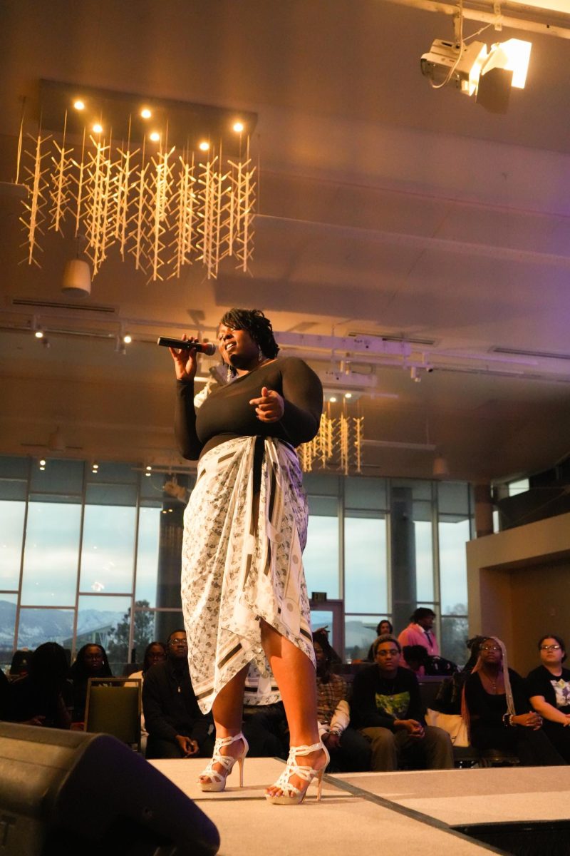 A woman sings into a microphone on the end of a runway stage in front of a crowd.
