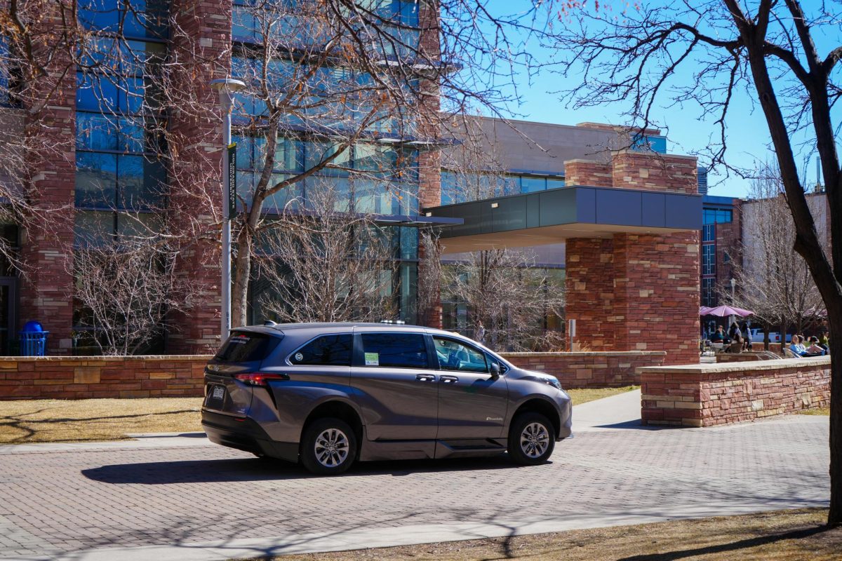 A car drives past a building on a college campus.