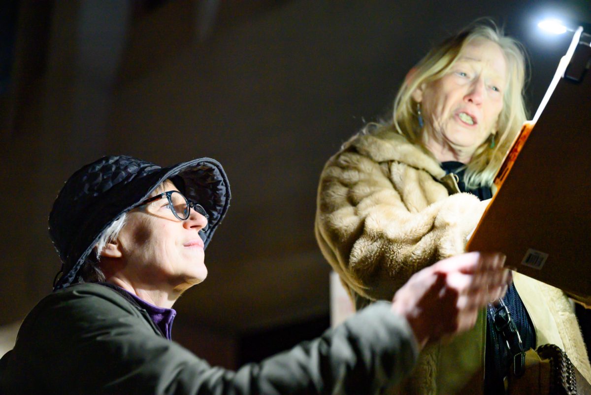 Kathy Maher, Vice President of the League of Women Voters of Larimer County, holds a light up to Rose Lew's page to help her see the speech she has written out during a protest outside the Fort Collins Post Office March 4.