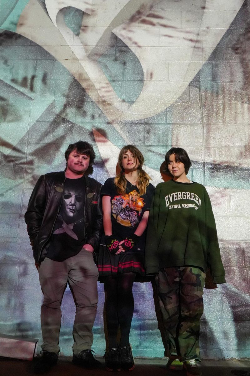3 band members pose in front of a mural.