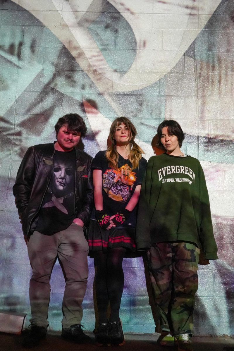 3 band members pose in front of a mural.