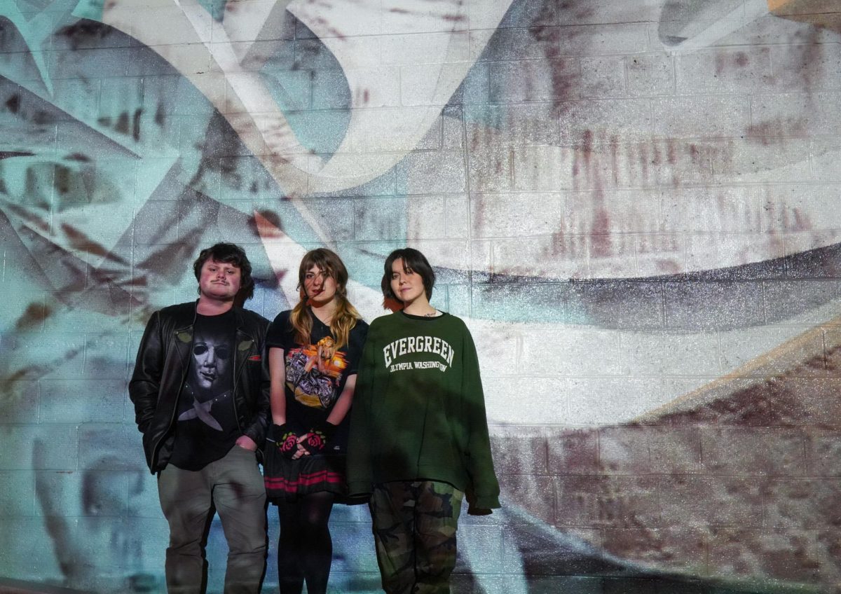 3 band members pose in front of a mural.