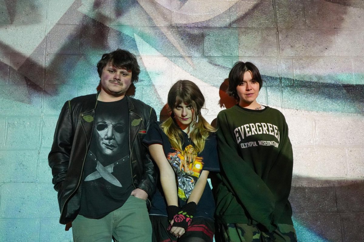 3 band members pose in front of a mural.