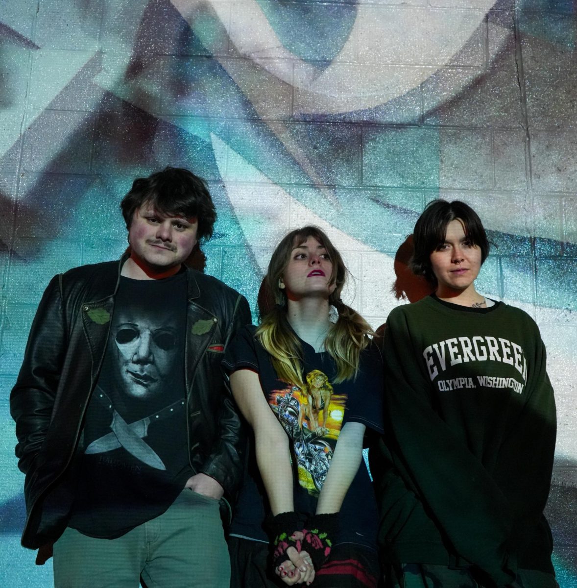3 band members pose in front of a mural.