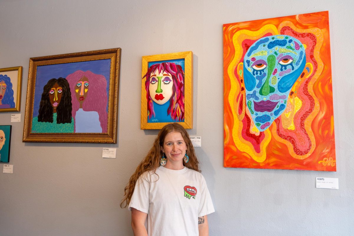 A woman stands in front of colorful paintings on display.
