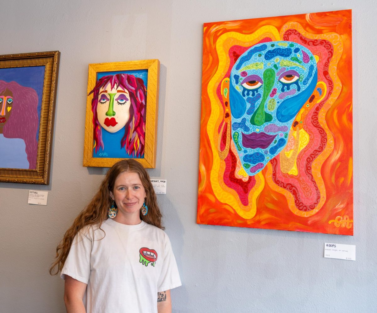 A woman stands in front of colorful paintings on display.