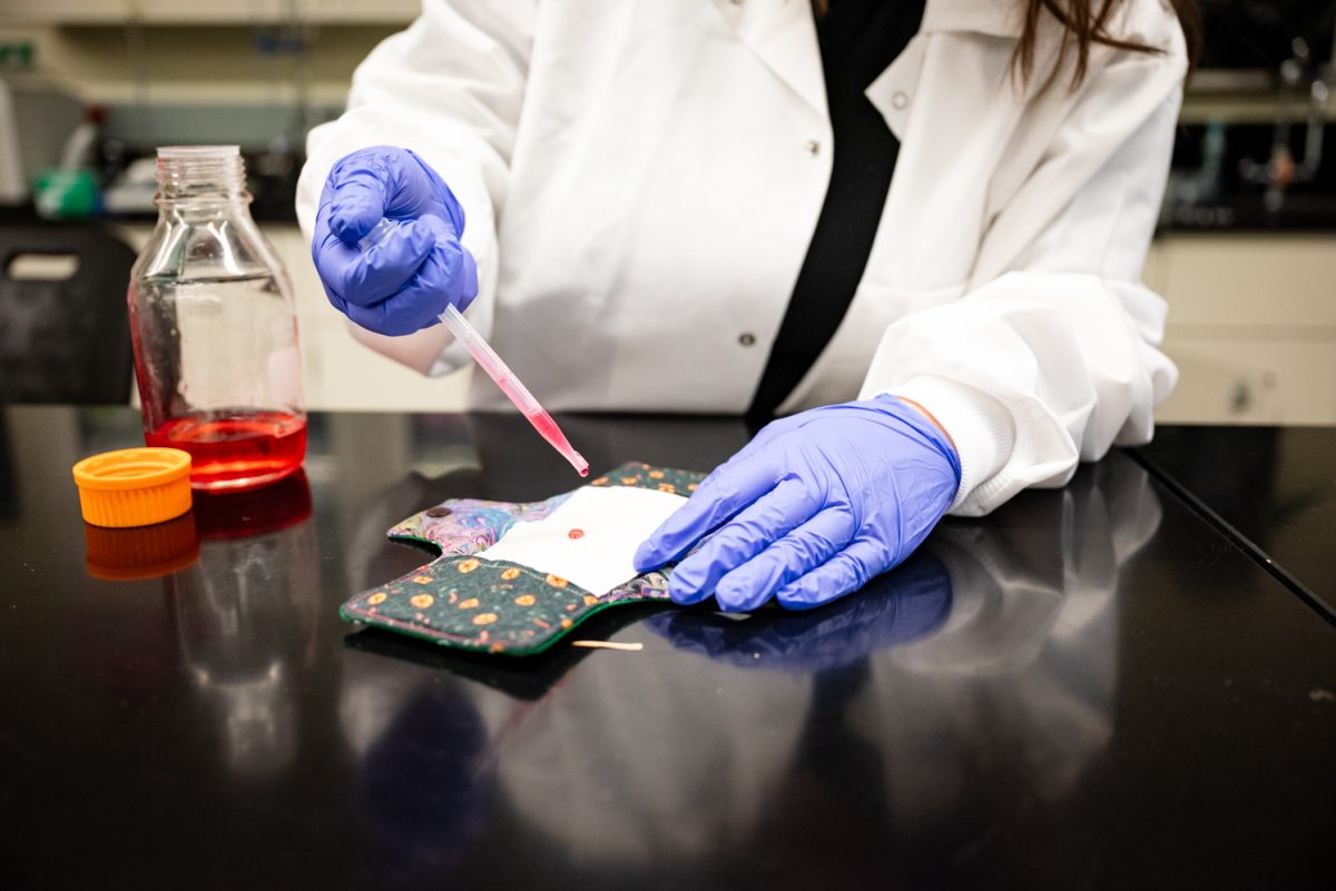 Shelby Ardehali demonstrates absorbency testing the team's biodegradable pads by using a dropper filled with a corn syrup, water and food dye solution April 25.