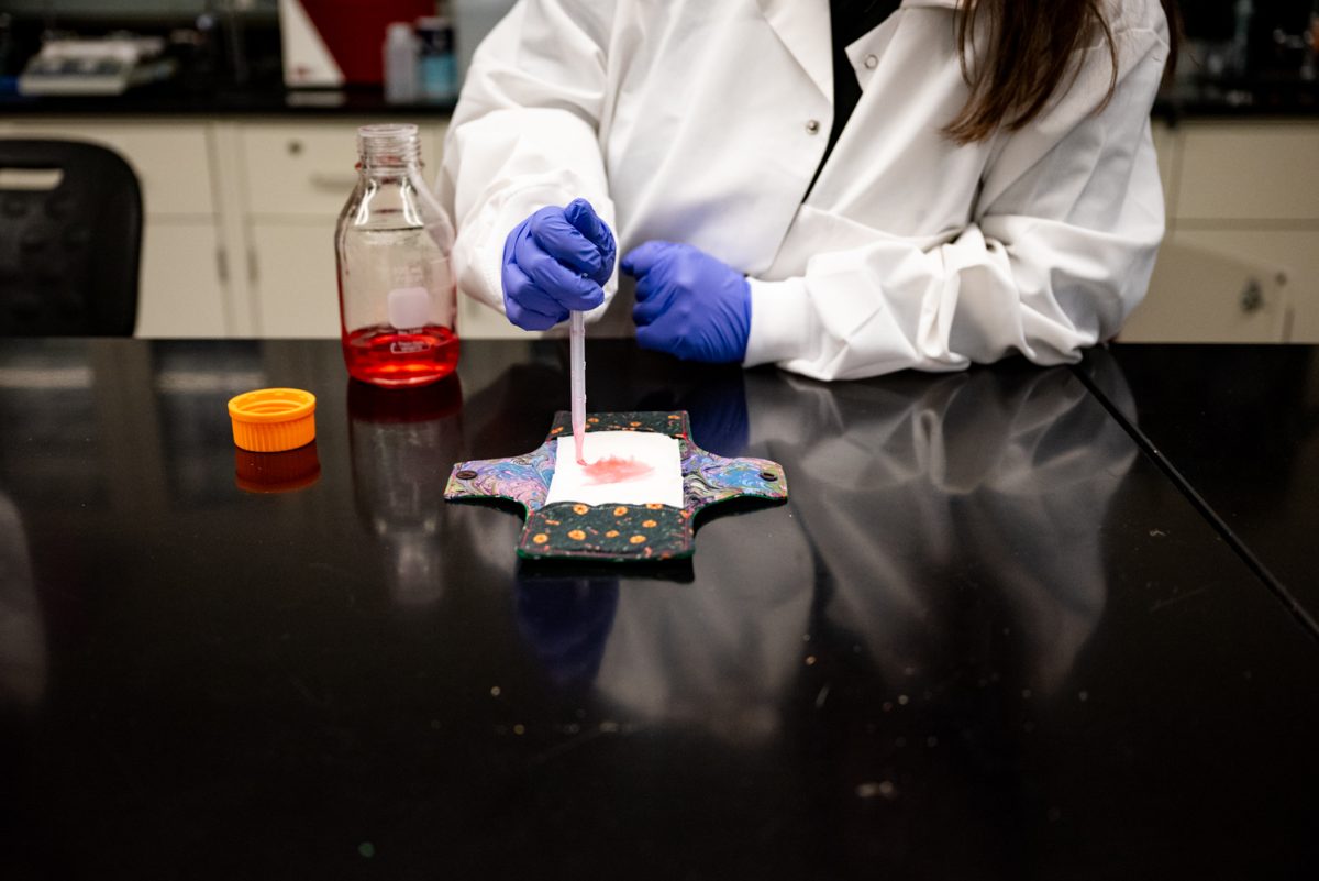 Shelby Ardehali demonstrates absorbency testing the team's biodegradable pads by using a dropper filled with a corn syrup, water and food dye solution April 25.
