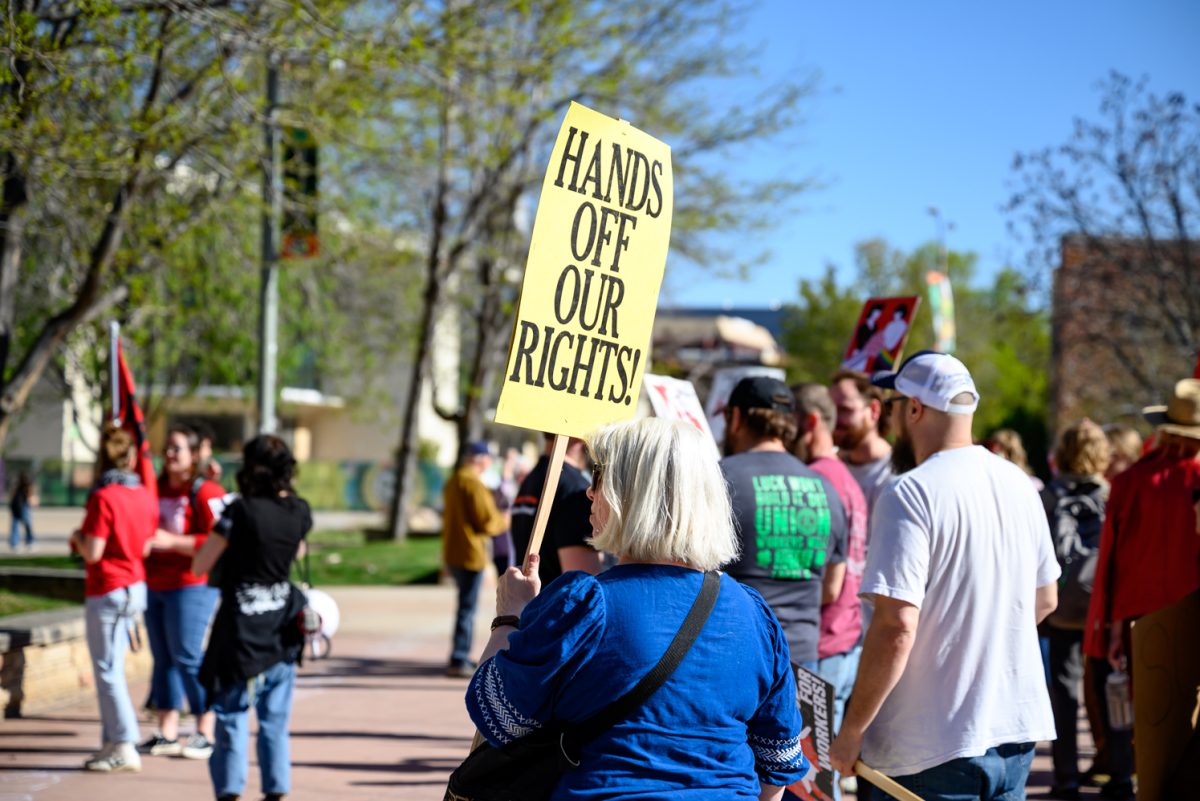 A protestor at the "March for Workers' Rights" protest holds up a sign that reads "hands off our rights" May 2. The protest began in the Lory Student Center plaza and moved through campus.