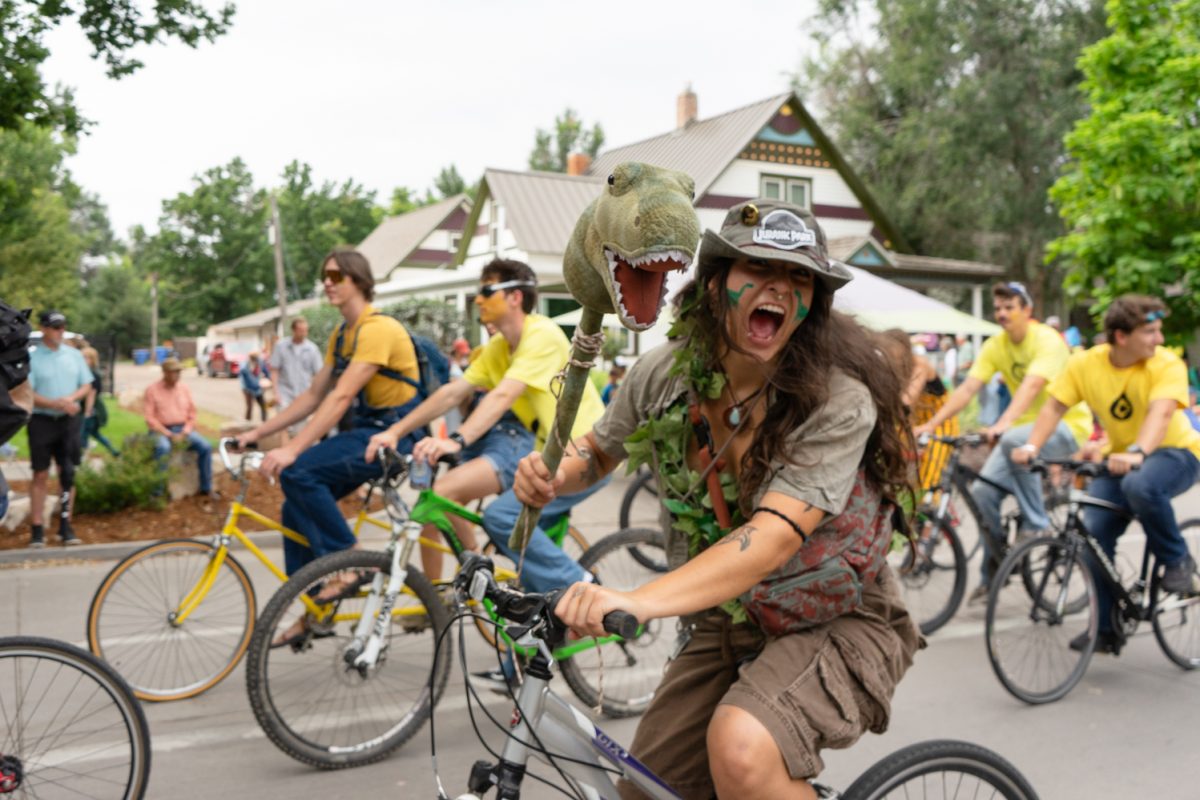 A young woman dressed in a "Jurassic Park"-themed costume holds a dinosaur head and enthusiastically roars while riding her bike in a crowded Fort Collins Tour de Fat cycling parade on Mountain Avenue Aug. 23. Tour de Fat is an annual event for community members to dress in costumes, bike and drink beer.