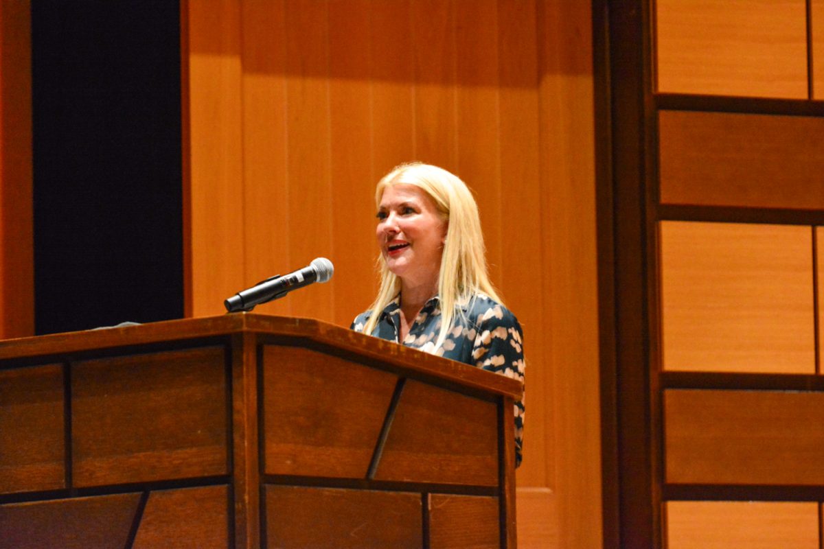 A woman giving a speech at a stand on stage.