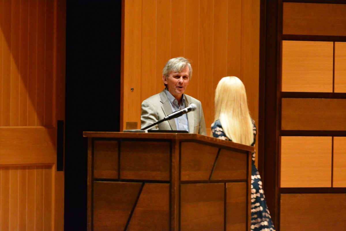 A woman shaking hands with a man as he walks onto the stage.