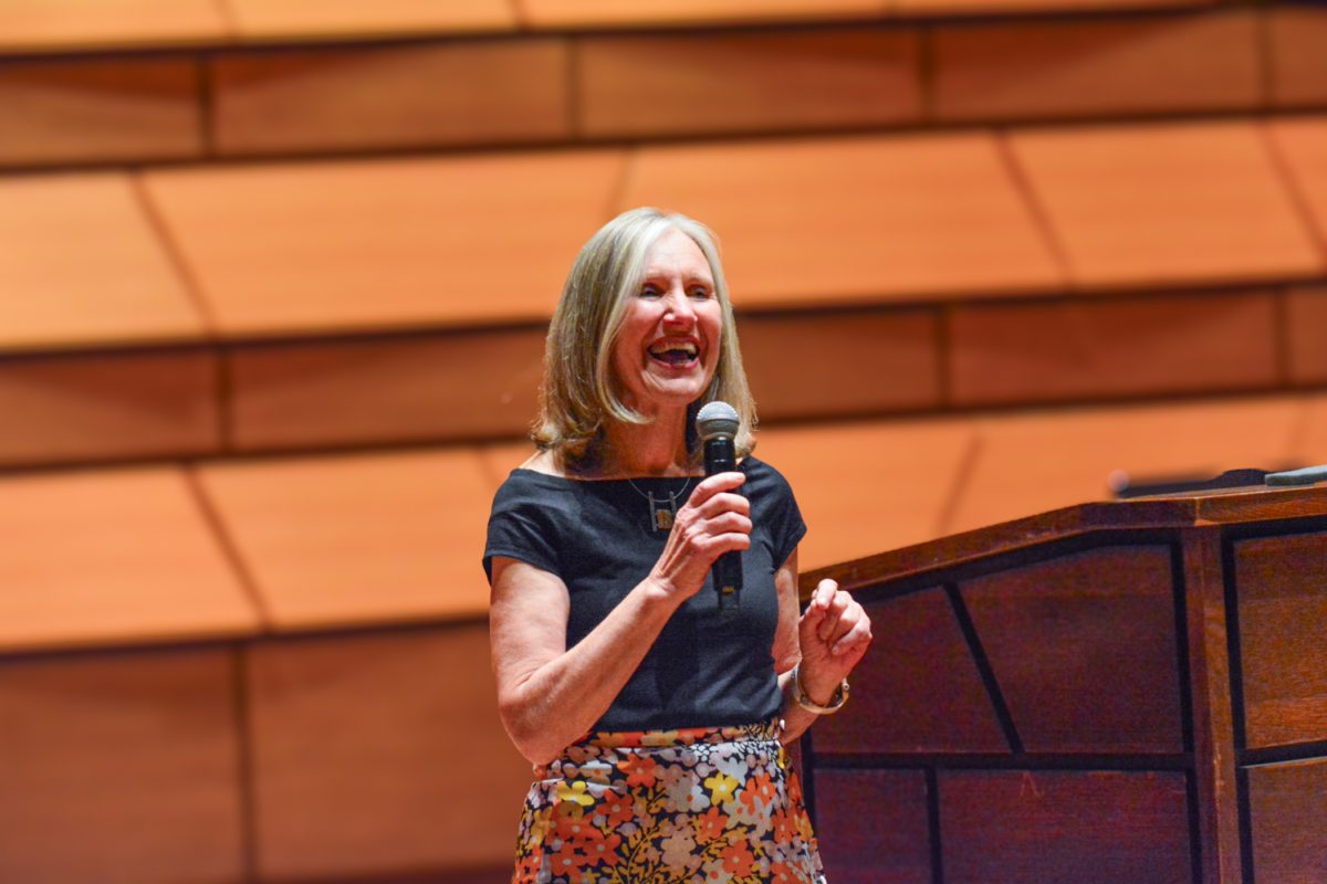 A woman smiling on stage with a microphone in her hand.