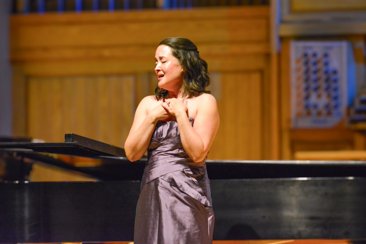 A woman singing to the crowd with her eyes closed and her hands on her chest.
