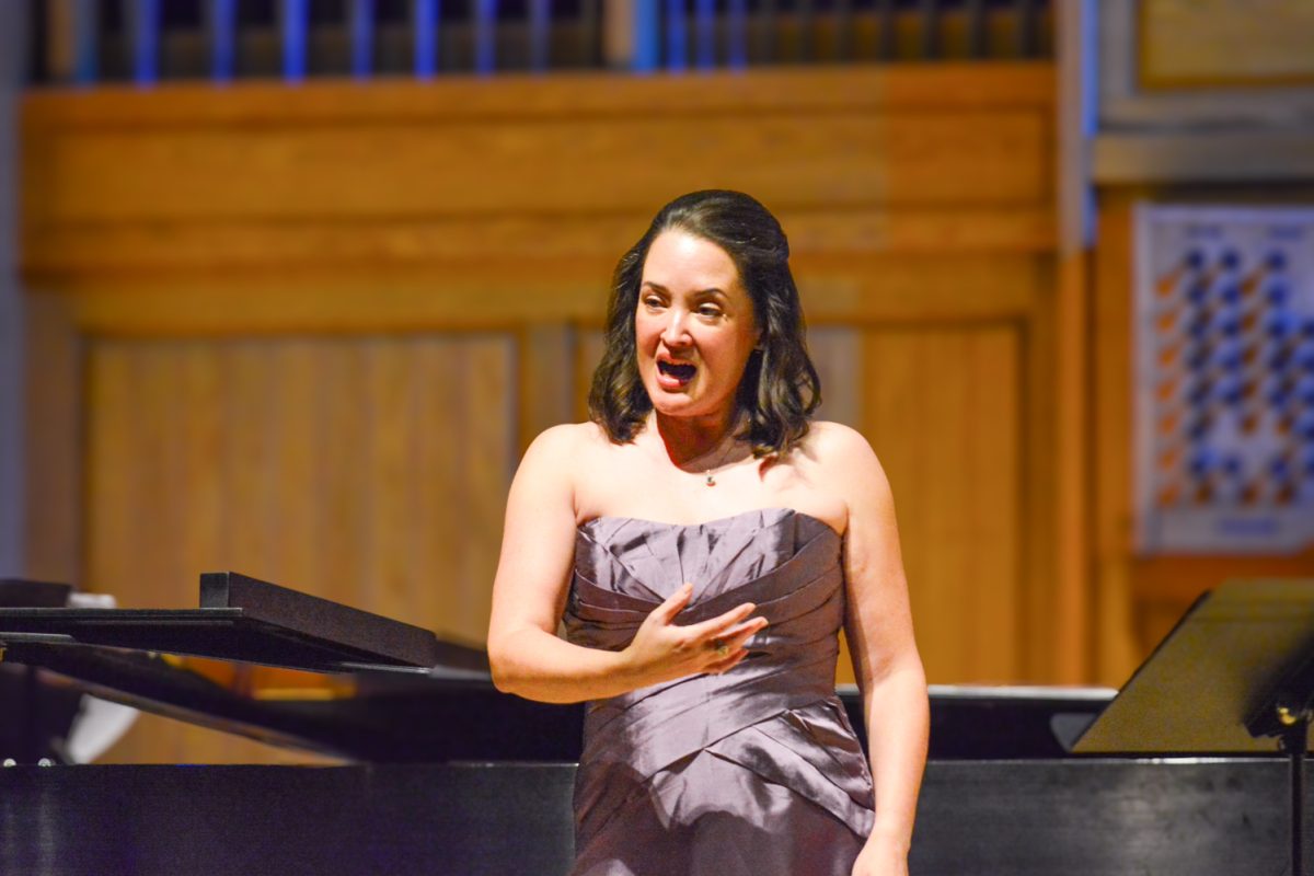 A woman in a purple dress expressively singing to the crowd while using hand gestures.