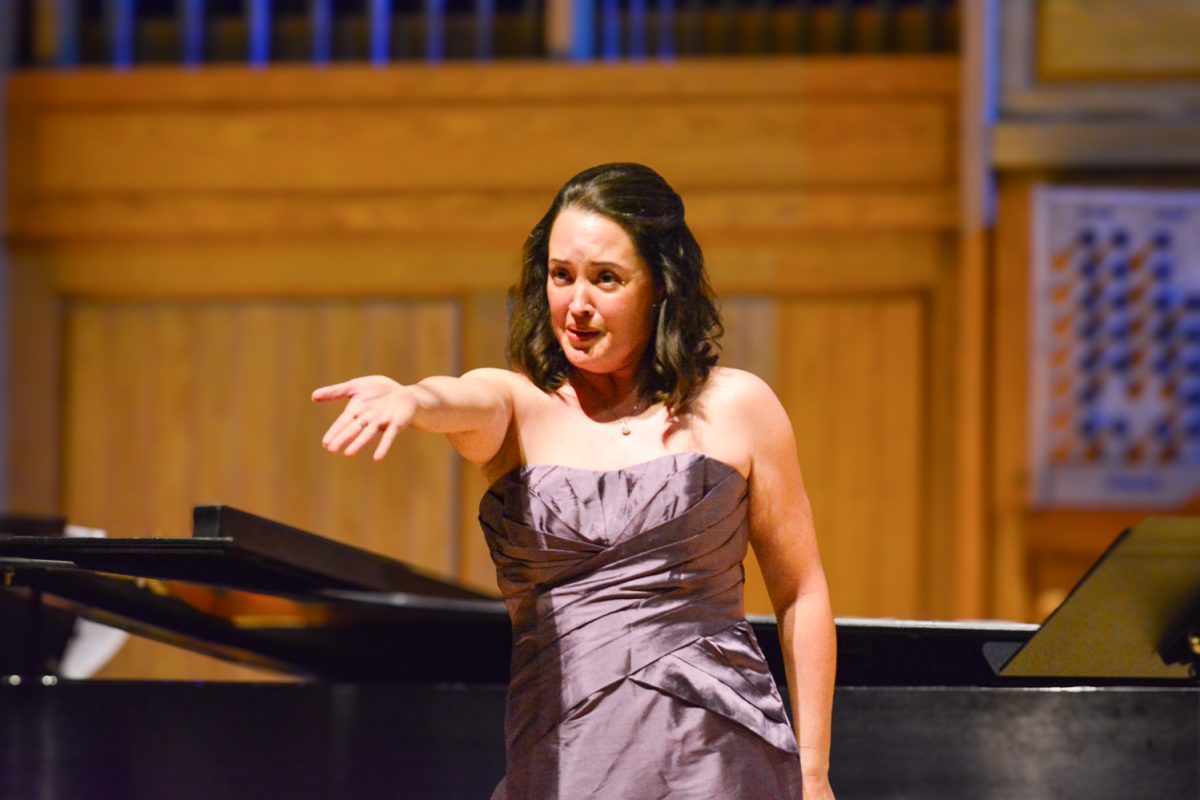 A woman in a purple dress holding out her hand to the crowd while singing.