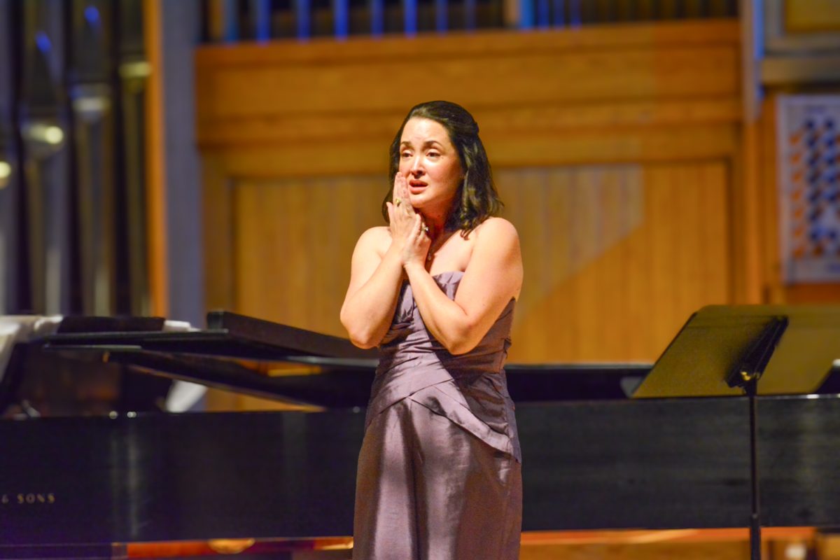 A woman in a purple dress holding her hands to her face as she sings.
